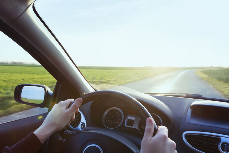 Driver holding a steering wheel on a rural road.